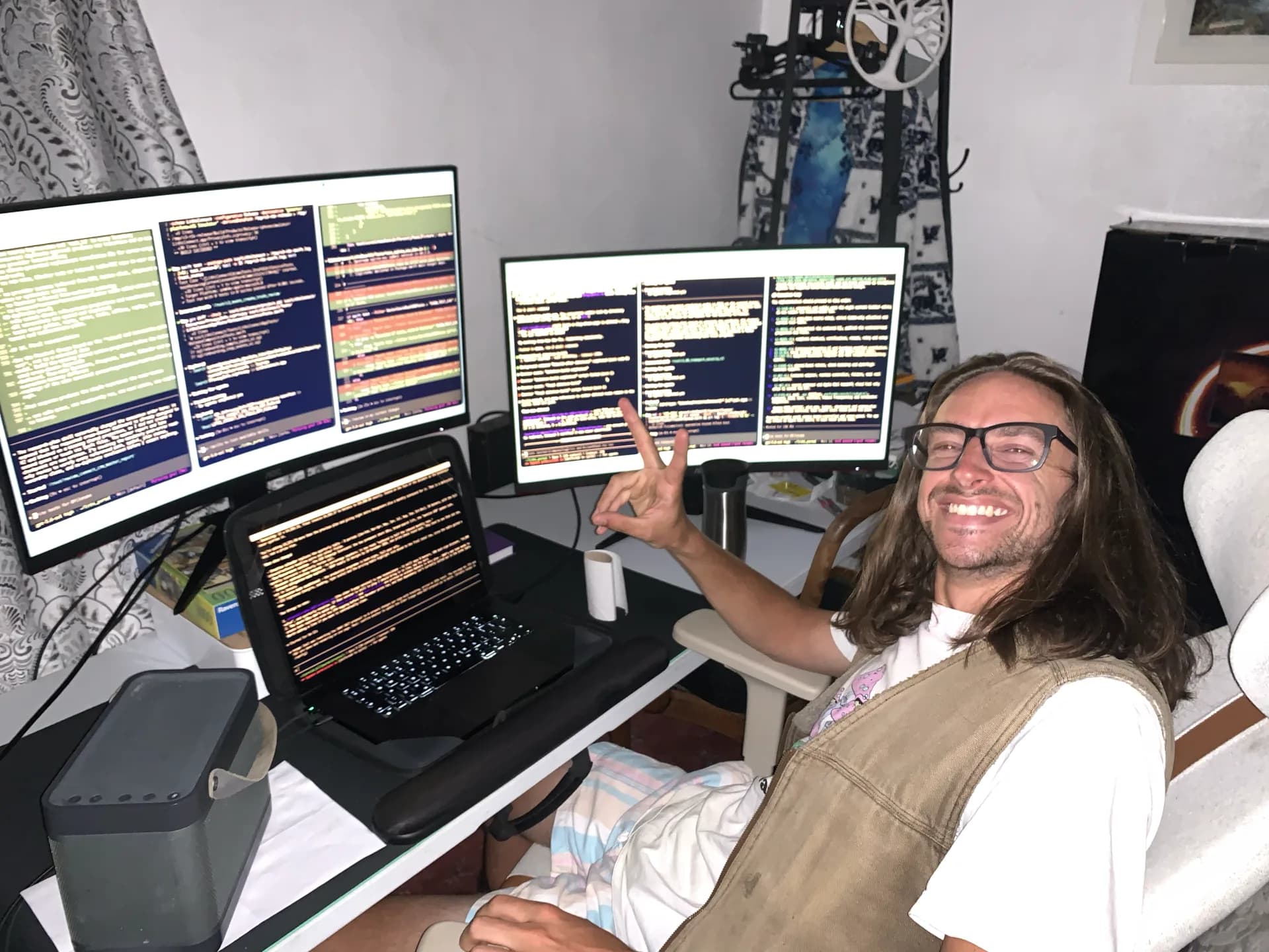 Ollie Hawkins beside two monitors and a laptop filled with terminal sessions during early parallel-agent experiments.